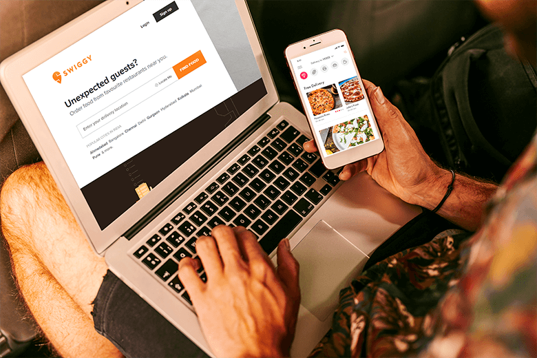 a man ordering food on swiggy on his laptop and tracking it's staus on his smartphone